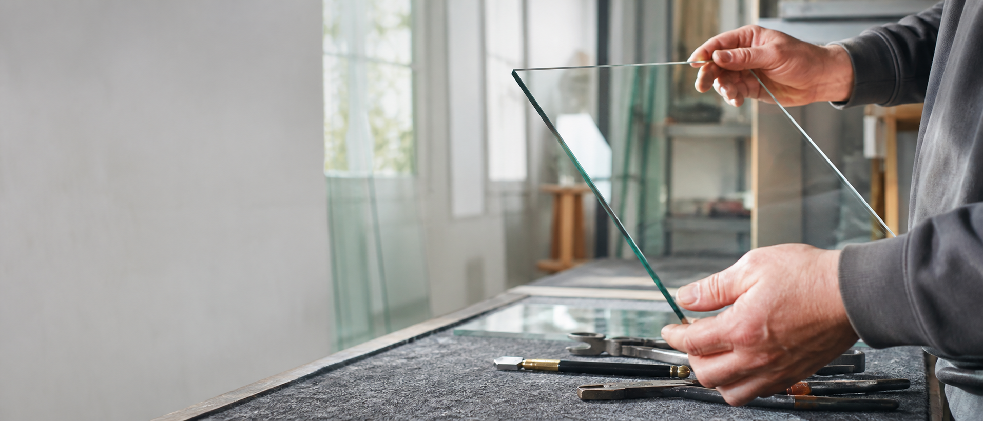 Hände prüfen eine Glasscheibe am Werkstattplatz